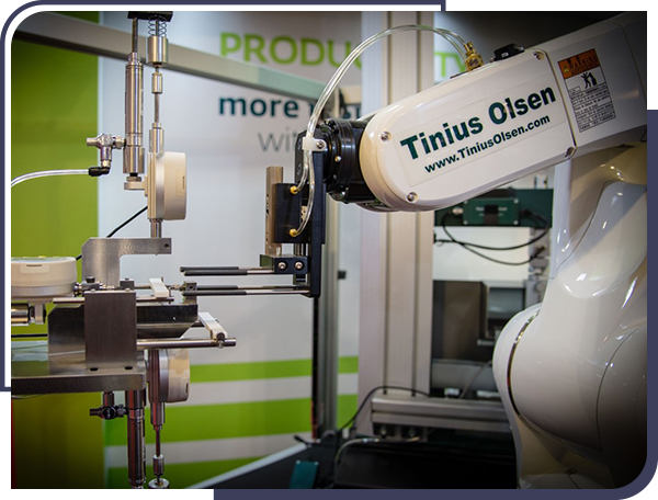 Tinius Olsen automated materials testing system showing robotic hand at the measurement station, a major data collection instance on this system.